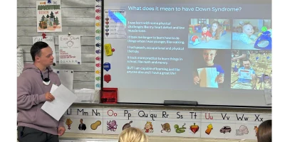 Matt holding a microphone and sharing a presentation about Down syndrome with a classroom